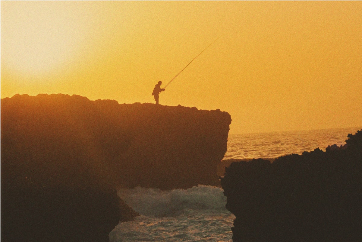 A fisherman on a rock on the beach in Morocco with sunset in the background