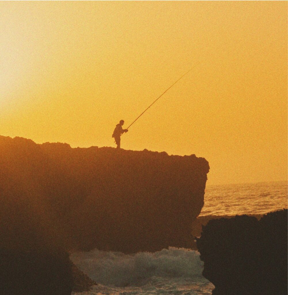A fisherman on a rock on the beach in Morocco with sunset in the background