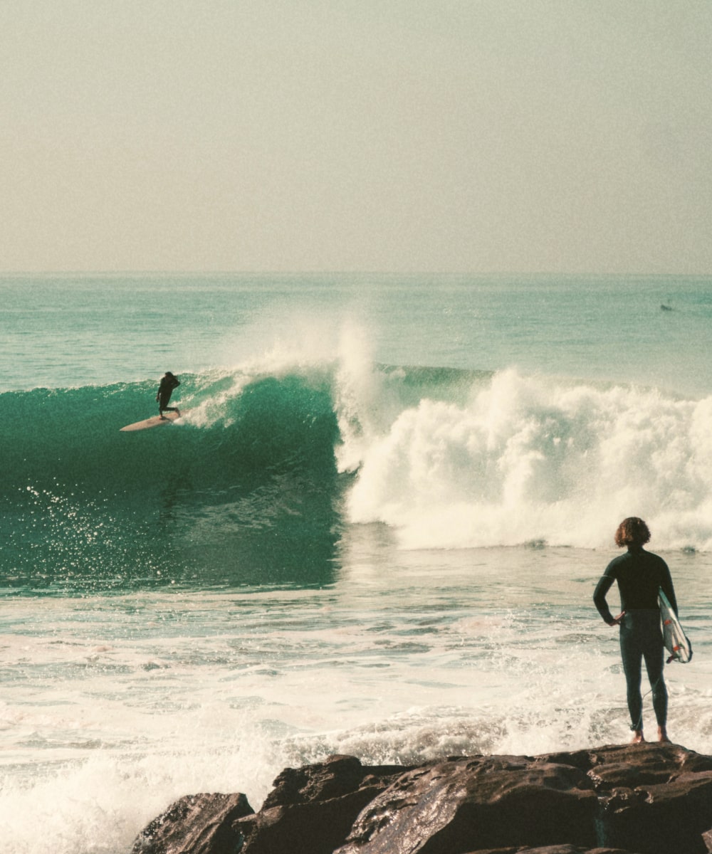 A Moroccan surfer watching another surfer in Anchor point, Taghazout